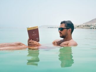 man wearing sunglasses reading book on body of water