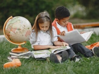 a boy and a girl sitting on grass with textbooks and a globe