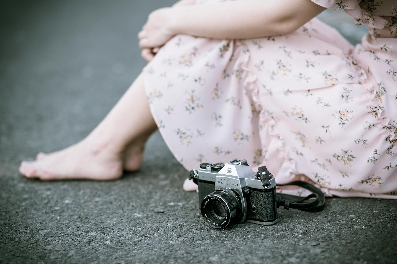 sitting woman wearing pink floral dress beside gray camera