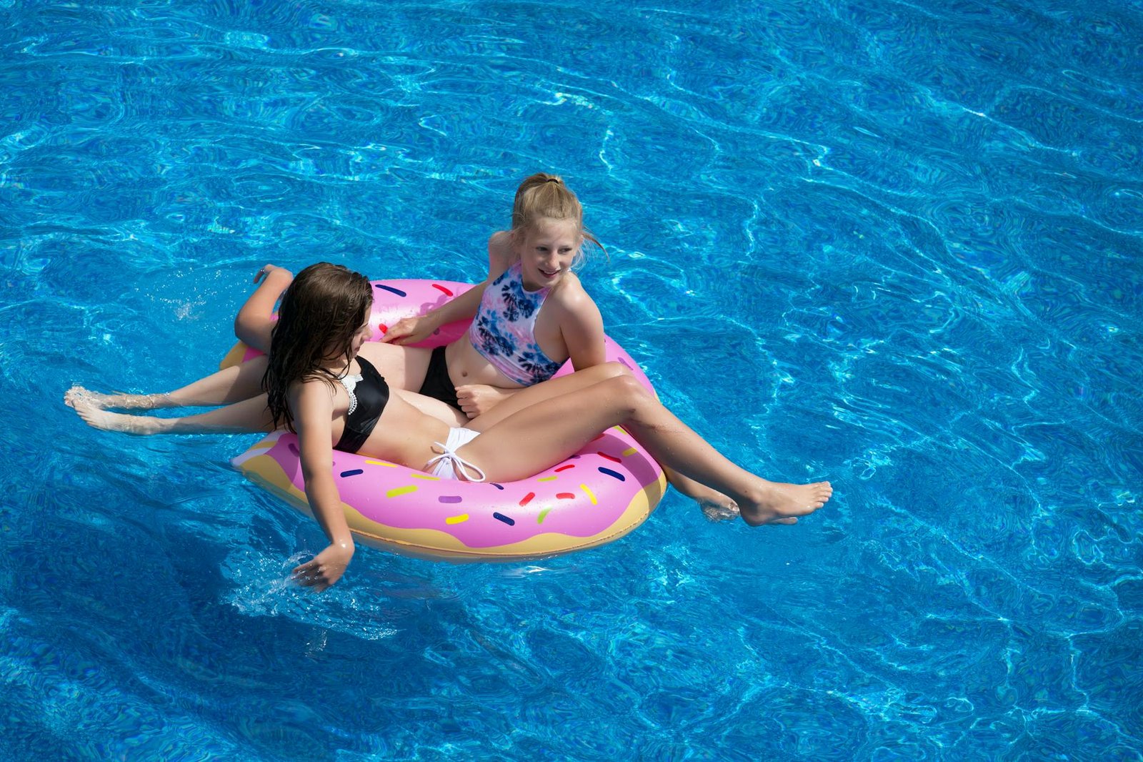 two girls sitting on pink doughnut pool float