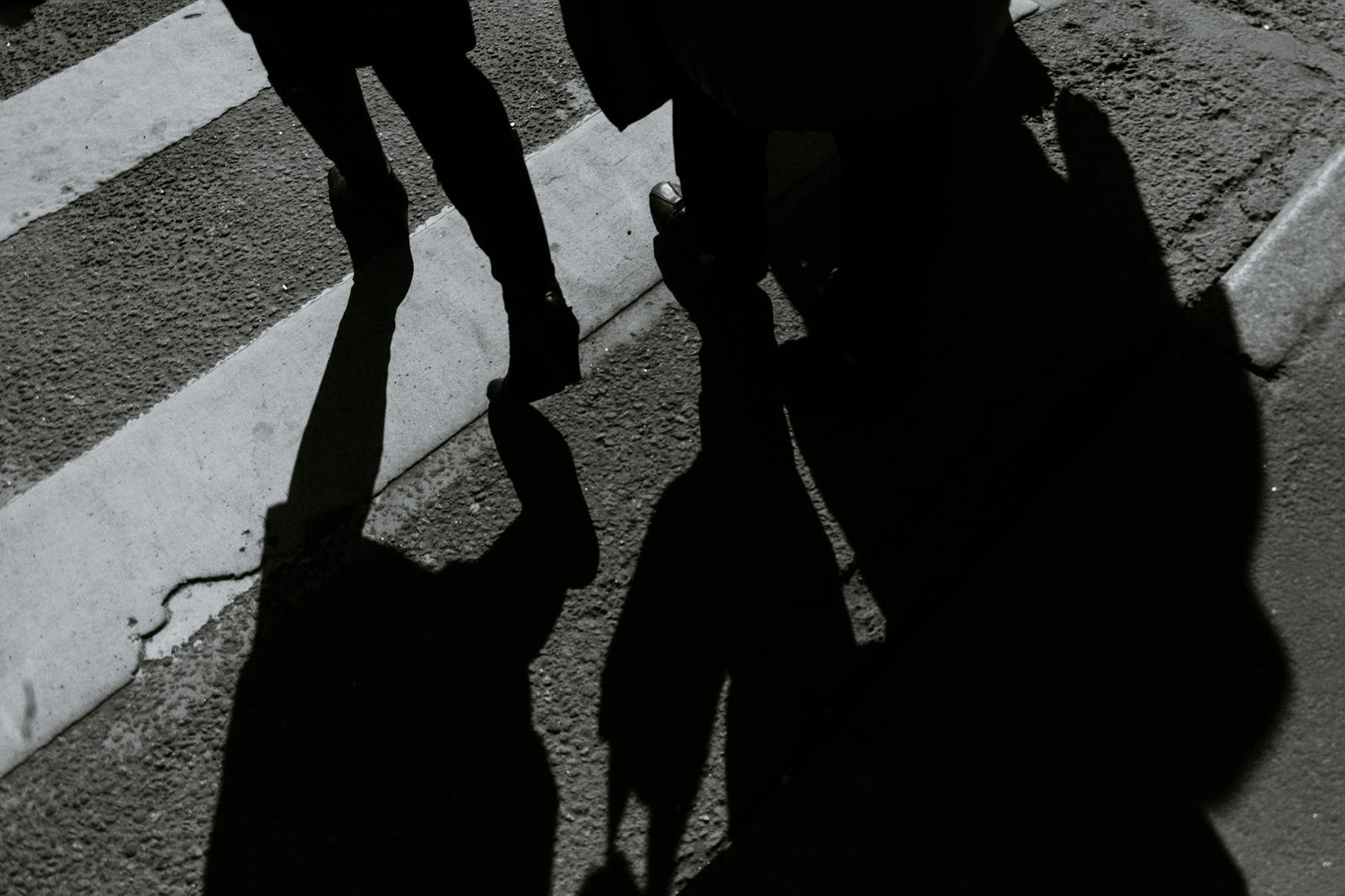 unrecognizable pedestrian silhouettes crossing asphalt road in town