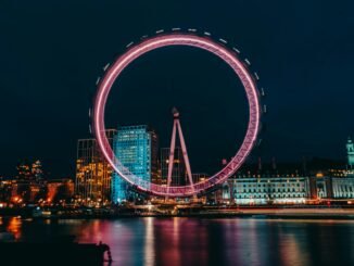 photo of luminous ferris wheel in modern city district on river bank at night