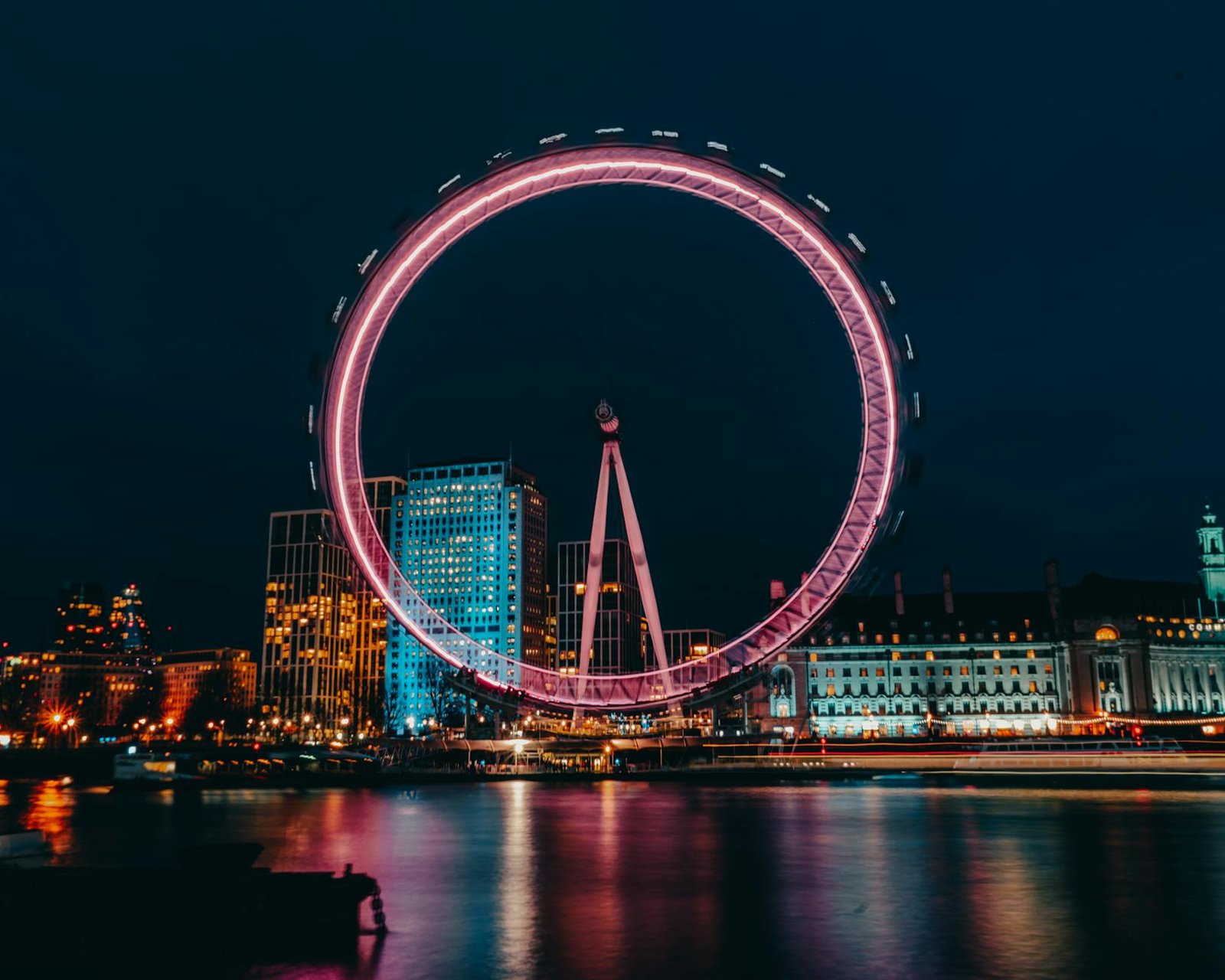 photo of luminous ferris wheel in modern city district on river bank at night